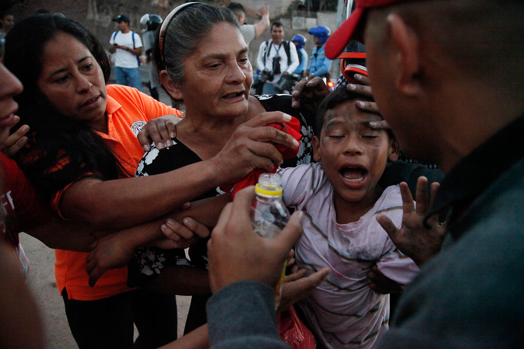A youth is assisted by bystanders as he reacts to tear gas